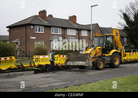 Yellow JCB and driver with kerb edgings in bucket  and workman laying them Stock Photo