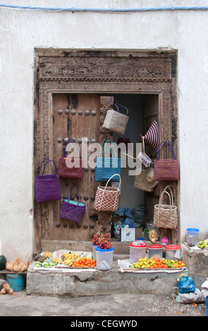 Colourful bags and fruit for sale, hanging on a traditional doorway in Stone Town, Zanzibar, Tanzania Stock Photo