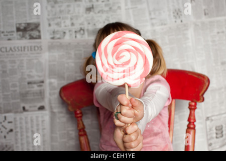 A girl holding a large striped lollipop, covering her face. Stock Photo