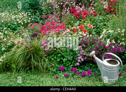 Metal watering can sits beside blooming flower border in back yard, Missouri USA Stock Photo