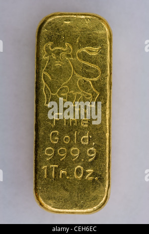 Pure one troy ounce gold bar with assay. Two silver bars in background ...