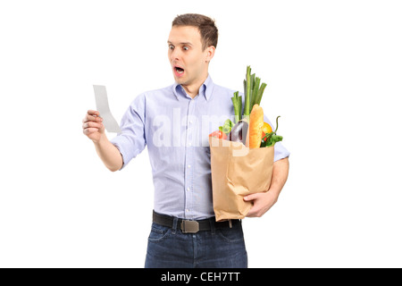 A surprised man looking at store receipt and holding a paper bag isolated on white background Stock Photo