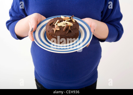 Overweight woman holding a plate with a chocolate cake on it. Stock Photo