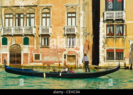 gondolier rowing a gondola with two tourists in it along a canal in front of a palazzo Venice italy ey europe Stock Photo