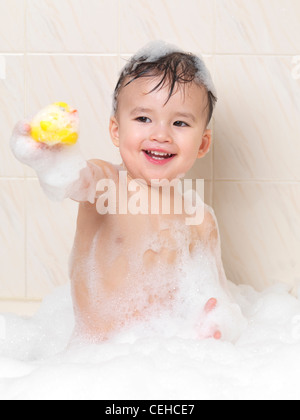 Two year old baby boy playing in a foam bath with a rubber duck