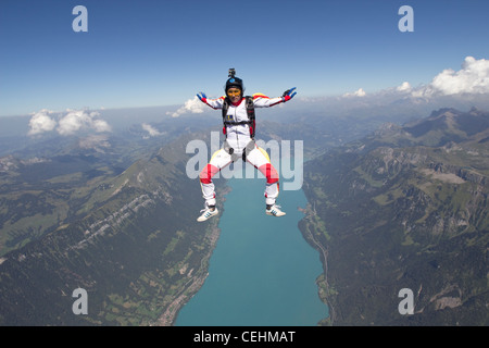 Skydiver girl is practice the sit position and flying free over a lake and nice mountain scenery with over 120 MPH. Stock Photo