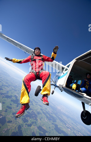 Skydiver girl is jumping out of an aircraft into the sit position and is flying free over nice landscape with high speed. Stock Photo