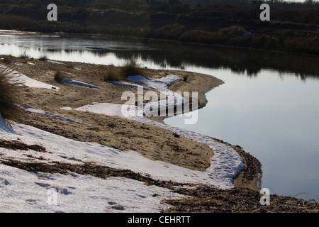 Snow lies on the ground next to a small lake at Benacre Nature Reserve near Kessingland in Suffolk Stock Photo