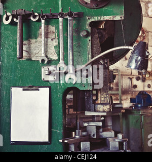 Assortment of various old tools hanging on a wall over workplace and a blank paper sheet as a copy space Stock Photo