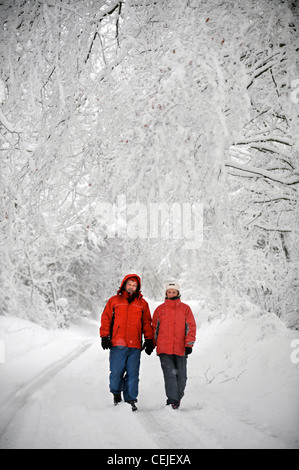 A couple in matching red winter coats walking in a Cotswold lane in snowy conditions UK Stock Photo