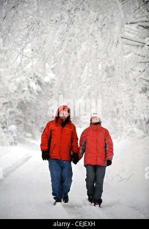 A couple in matching red winter coats walking in a Cotswold lane in snowy conditions UK Stock Photo
