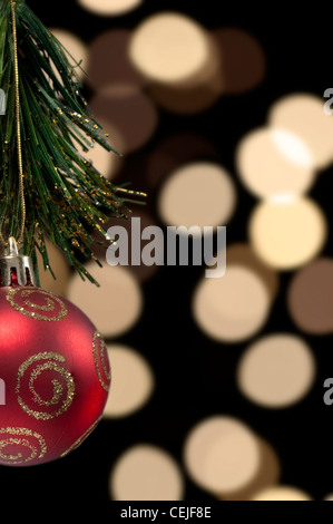 A red Christmas tree ball decoration against a background of out of focus blurred Christmas tree lights Stock Photo