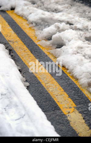 A double yellow line road marking emerges from under thawing snow UK Stock Photo