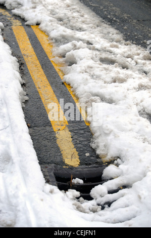 A double yellow line road marking emerges from under thawing snow UK Stock Photo