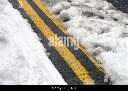 A double yellow line road marking emerges from under thawing snow UK Stock Photo