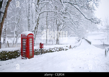 Linton Village West Yorkshire UK. A snow covered landscape photo with the bright red Telephone Box and Post Box standing out. Stock Photo