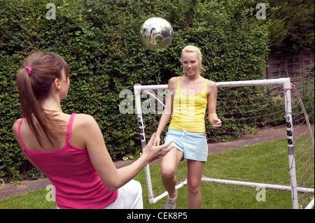 Two females playing football in garden both knees raised keeping football in air, back view of female on left brunette hair Stock Photo