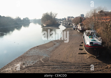 Winter low tide on the River Thames, London, with house boats on the Brentford bank. Viewed from Kew Bridge looking westwards. Stock Photo