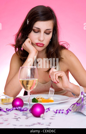 Female long brunette hair diamante hairclip wearing gold halterneck top sitting at table in front of plate small pieces of Stock Photo