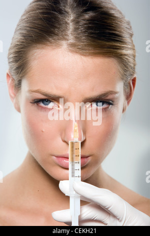 Female with blonde hair worn tied up having Botox injection in her nose Stock Photo