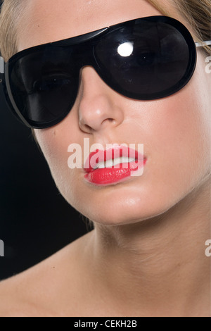 Female with blonde hair wearing worn tied up wearing bright red lipstick and large black sunglasses Stock Photo
