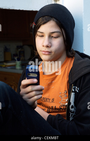 Teenage boy wearing black beanie orange t shirt and black hooded top and black jeans sitting on window frame looking down at Stock Photo