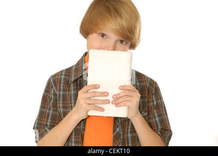 Eleven year old boy holding up a tablet computer or eBook reader, or hiding behind it and peeking over the top. Stock Photo