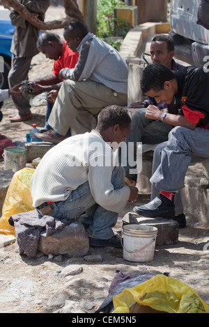 Addis Ababa, Ethiopia. 'Shoe shine boy'. Young man cleaning and polishing leather shoes of people sitting on city's road side. Stock Photo