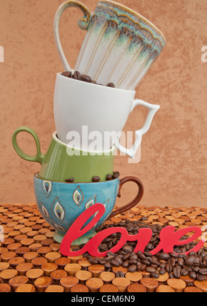 Four Coffee Cups Pile on Top of Each Other with coffee beans and the word love on the wooden counter and brown stucco background Stock Photo