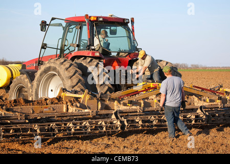 Three farmers work to set up a secondary tillage implement during field preparation operations prior to planting cotton / USA. Stock Photo