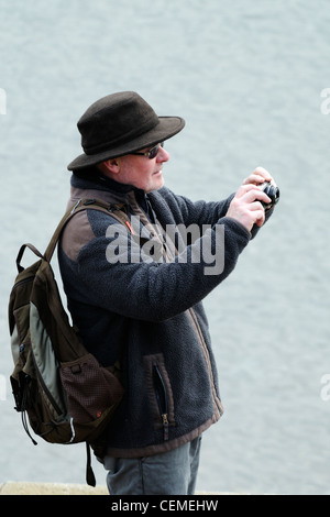 A middle aged man takes a photo whilst standing on the seawall at Dawlish Stock Photo