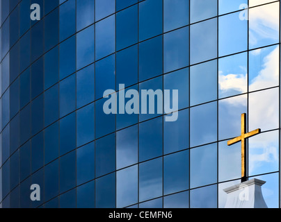 A golden Christian Cross in front of a modern glass building in New York City, USA Stock Photo