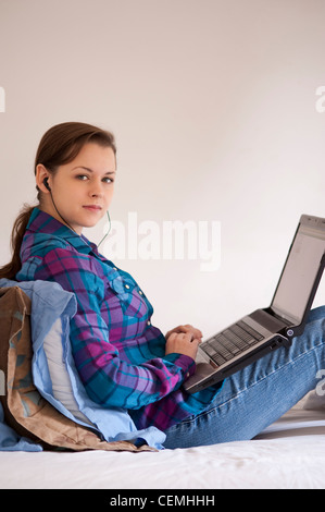 College student sitting on bed using a laptop in dorm room before classes Stock Photo