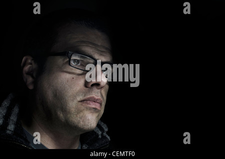 Low-key portrait of a middle-aged man wearing glasses looking attentively at a computer screen. Stock Photo