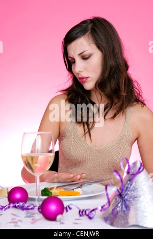 Female long brunette hair diamante hairclip wearing gold halterneck top sitting at table in front of plate small pieces of Stock Photo