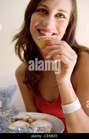 Female long wavy brunette hair wearing diamante bracelet and red halterneck dress, leaning forward holding mince pie from Stock Photo