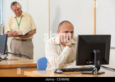 Hispanic engineering student studying computer display in a classroom with professor in background Stock Photo