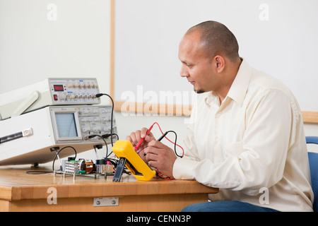 Hispanic engineering using multimeter probes to measure circuit characteristics in lab experiment in a classroom Stock Photo
