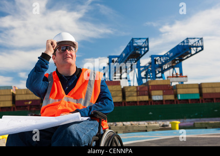 Transportation engineer in a wheelchair studying plans at shipping port Stock Photo