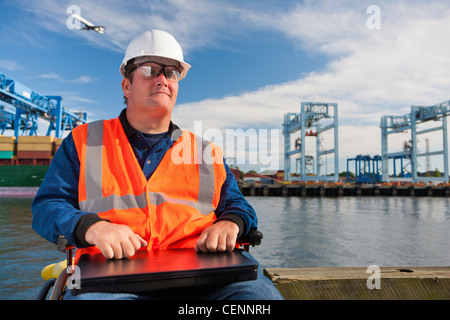 Transportation engineer in wheelchair with a laptop at shipping port Stock Photo