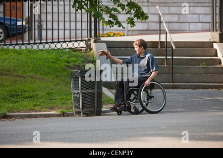 Man with spinal cord injury in a wheelchair putting trash in receptacle at public park Stock Photo