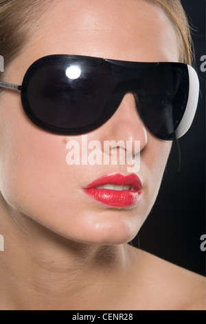 Female with blonde hair wearing worn tied up wearing bright red lipstick and large black sunglasses Stock Photo