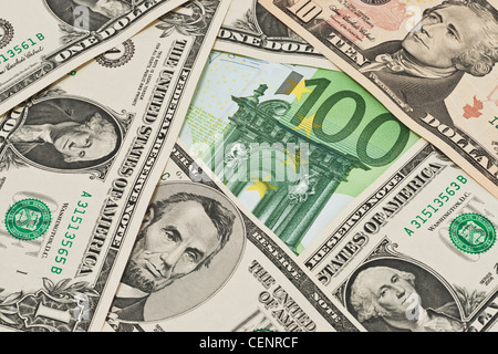 Many U.S. Dollar bills lying side by side. In the middle lies a 100 Euro bill. Stock Photo