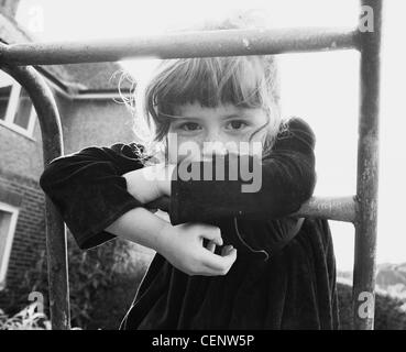 Female child leaning against climbing frame in garden outside house Stock Photo