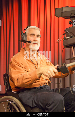 Man in wheelchair with muscular dystrophy using a TV camera and a teleprompter in studio Stock Photo