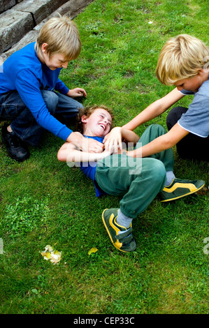 Two male children tickling another male child Stock Photo