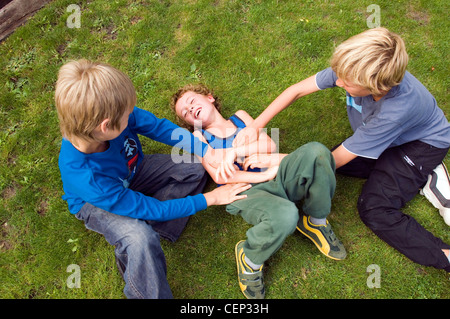 Two male children tickling another male child Stock Photo