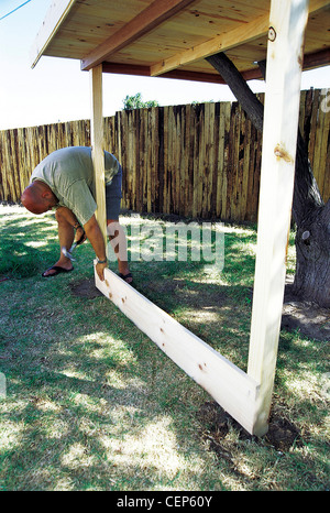 FORBuild a Tree House Step Male hammering nails into the reinforcing plank of wood to the base of the tree house Stock Photo