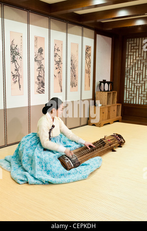 a young Korean woman playing a Korean traditional musical instrument gayageum or kayagum wearing Korean traditional costume Stock Photo