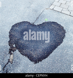 Wet dark stain of puddle on textured asphalt footpath in shape of heart, conceptual abstract background Stock Photo